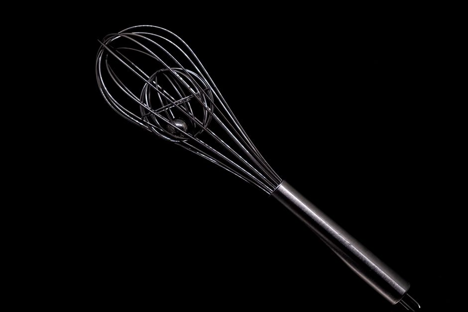 Elegant close-up of a stainless steel whisk against a black backdrop, showcasing its sleek design.